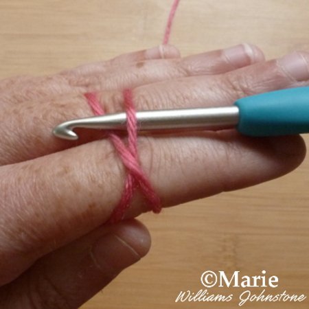 Placing a crochet hook under the crossed strands of yarn